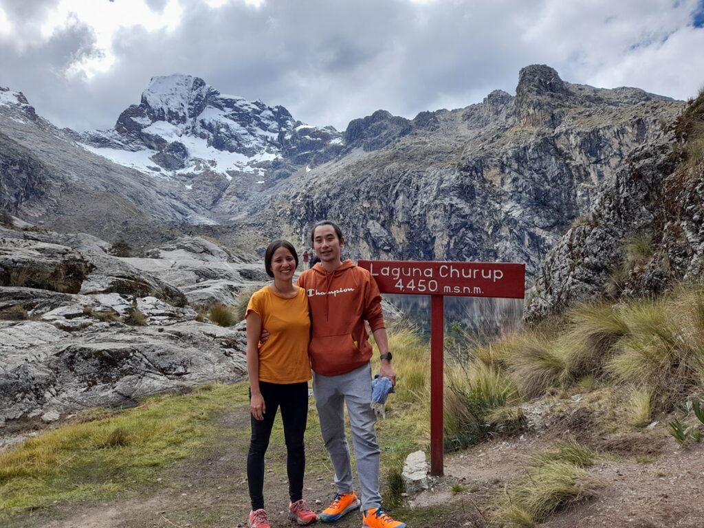 My partner and I next to a sign indicating that we arrived at lake Churup, at 4500 meters above sea levels. Snow-capped mountains in the background.