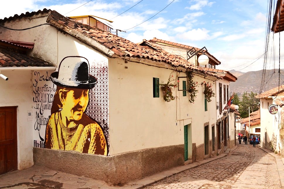 Streets of Cusco. Tiled roofs, cobblestone streets, and a mural painting of a woman in traditional clothing from Cusco.