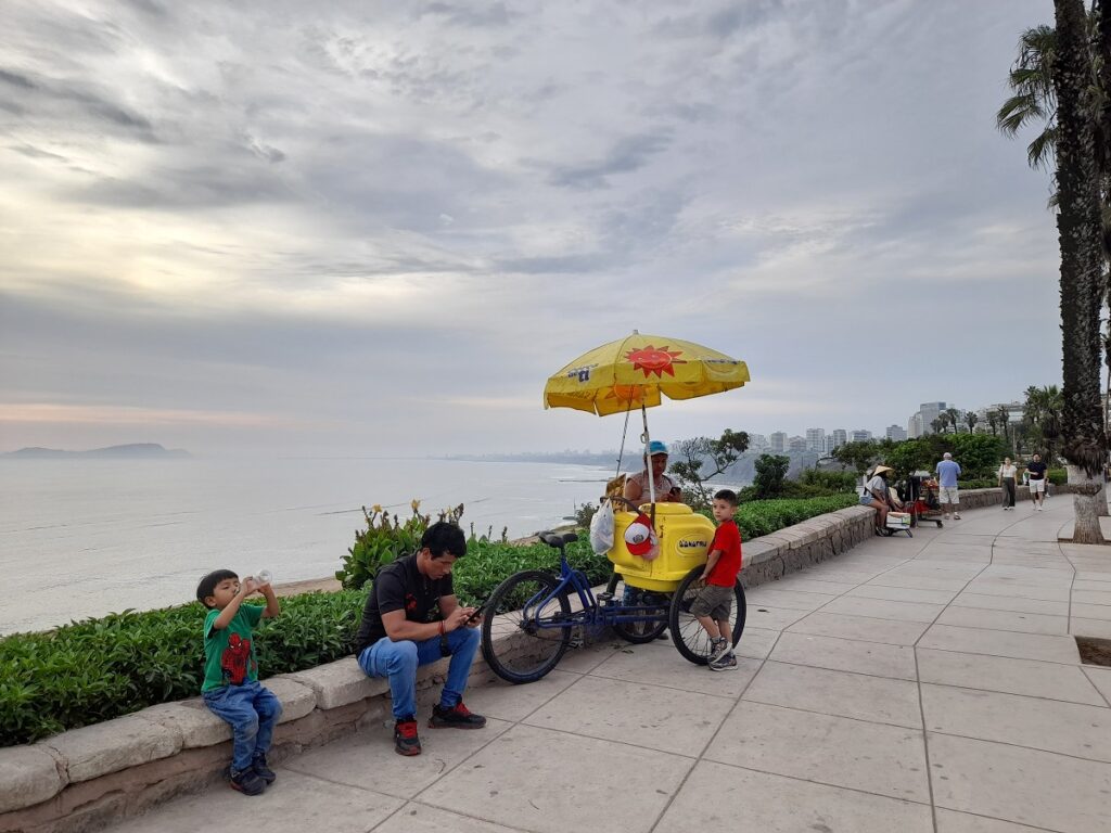 The boardwalk, people sitting and an icre-cream vendor. The sea on the background