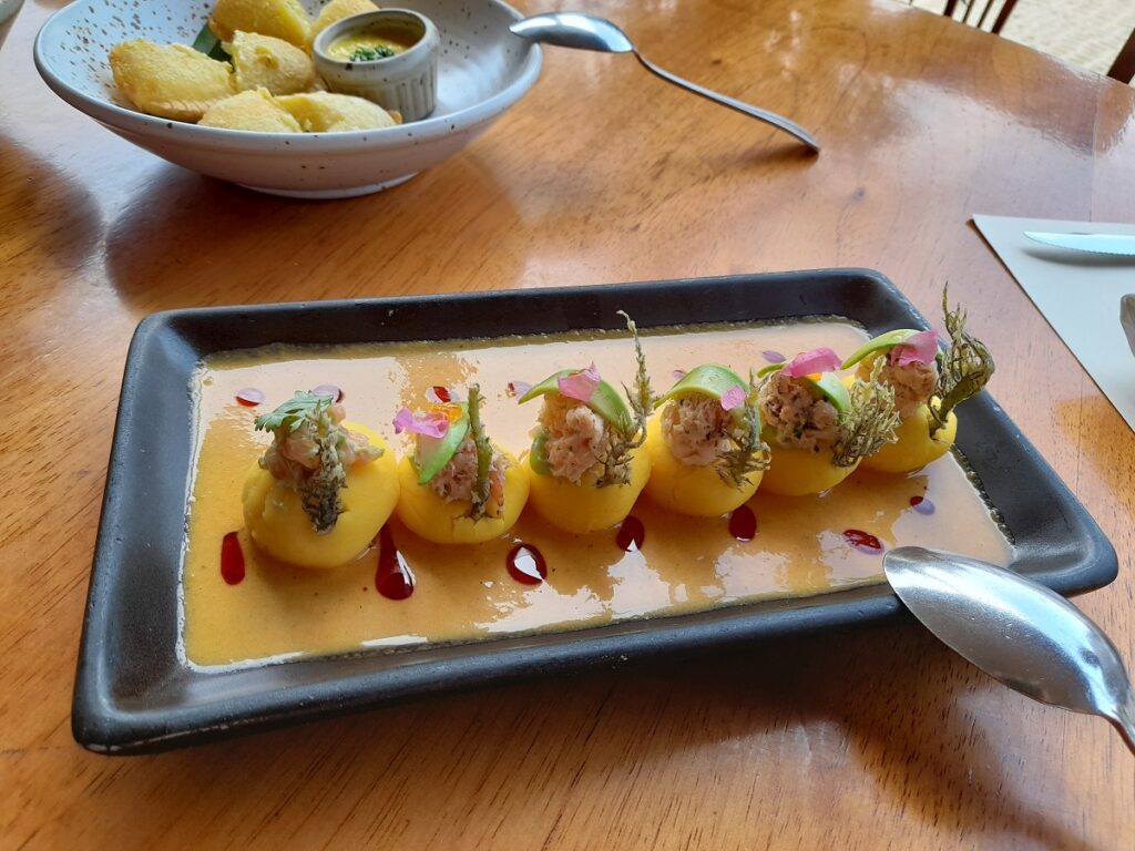 Causa servings, topped with flower petals, served on top of an orange sauce.