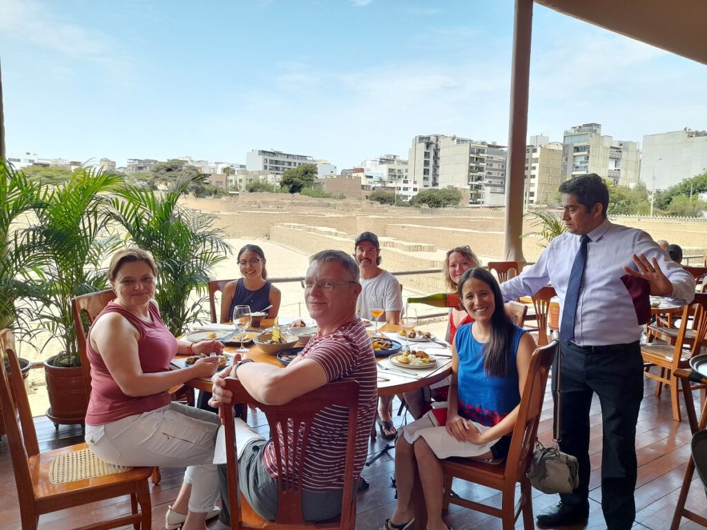 The group at our food tour, including the guide, having lunch by the ruins in Miraflores, Lima. A waiter is puring wine on a glass.