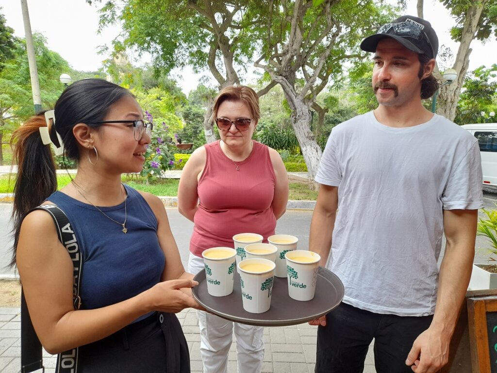Our guide at this food tour holding a tray of lucuma shakes, offering it to the tour guests. A street of Barranco, Lima, in the background. 