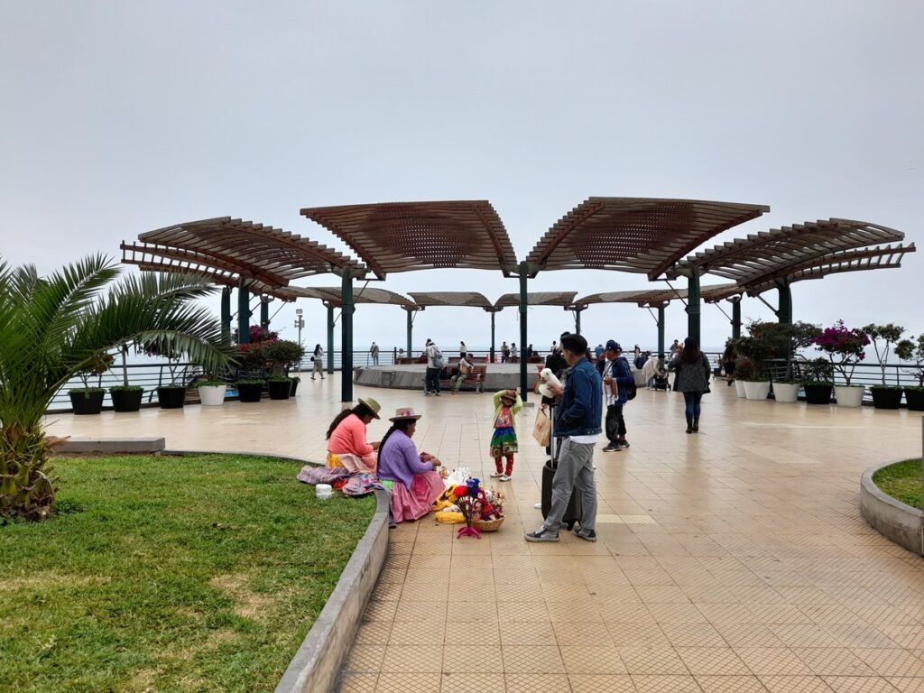 Women in traditional attire selling souvenirs at Parque Salazar to tourists under a grey sky, an authentic August experience in Lima.