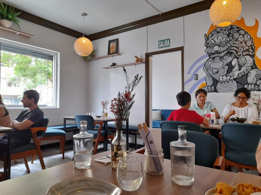 Patrons dining at Asianica, a vegetarian restaurant in Lima, Peru, with stylish interior decor featuring a mural of a mythical creature, cozy blue seating, and natural light.