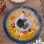 "Exquisite vegetarian cebiche presentation at Asianica restaurant in Lima, with a creative assortment of marinated tofu, mushrooms, and corn, garnished with a dramatic smoke effect for an enhanced sensory experience, accompanied by crispy fried roots.
