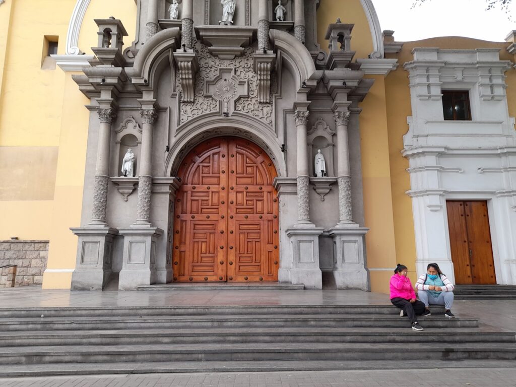 Historic yellow church in Barranco with women in winter attire, a serene June scene for travelers seeking the quieter side of Lima.
