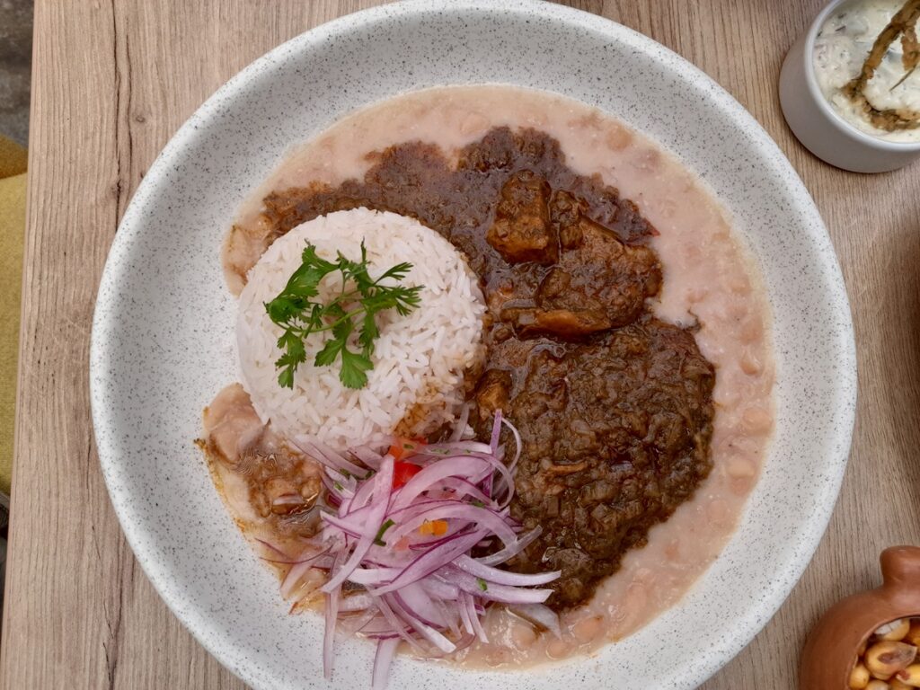 raditional Huatia Surcana made vegan at Gastronomia Vegana in Lima, featuring a rich and savory seitan stew paired with white rice and beans, garnished with red onion slivers, all served in a speckled ceramic bowl, providing a plant-based take on this Peruvian culinary delight.